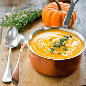 Pumpkin soup and pumpkin with 2 spoons beside saucepan