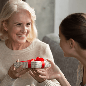 grandmother receiving a gift from her grand daugher wrapped in white package with red ribbon