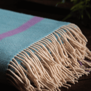 close up image of merino wool and cashmere throw aqua and raspberry look great on bed or sofa