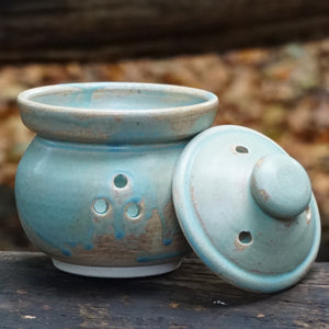 Garlic keeper pot with lid off and placed beside pot on dark surface