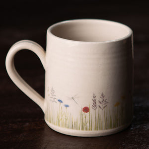 The meadow mug is hand crafted with a meadow and dragonfly scene hand painted onto each mug